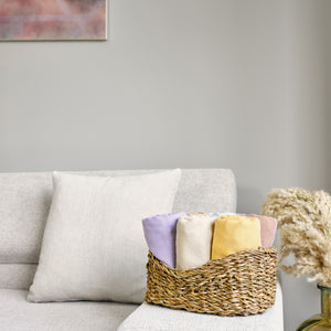 Woven basket with folded towels on a gray sofa against a neutral wall.