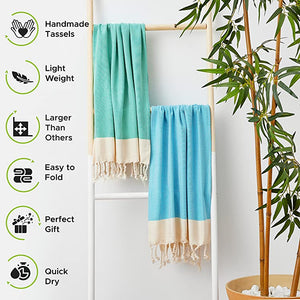 Two turquoise towels with white fringe hanging on a rack, surrounded by greenery.
