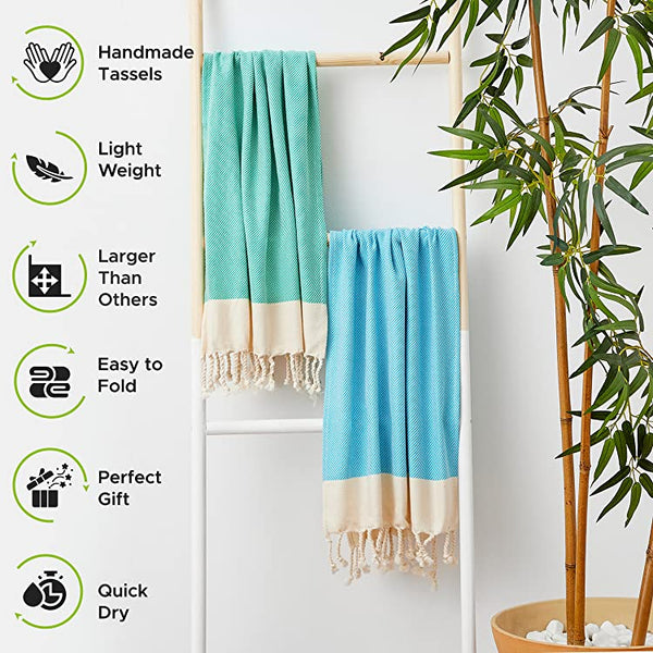 Two turquoise towels with white fringe hanging on a rack, surrounded by greenery.